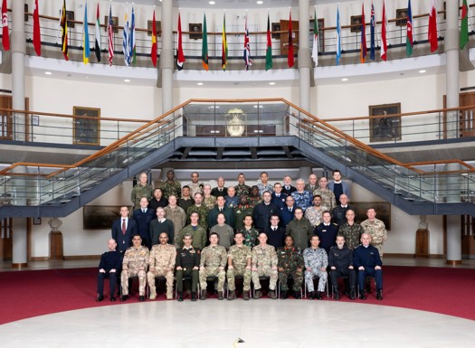 The whole International Defence Attache party in a group event photo in the forum surrounded by international flags above them.
