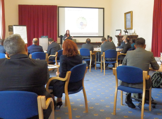 A group of people sat around tables in a syndicate room while being presented to.
