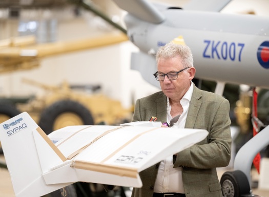 A person holds a small white drone labeled in front of a larger aircraft marked