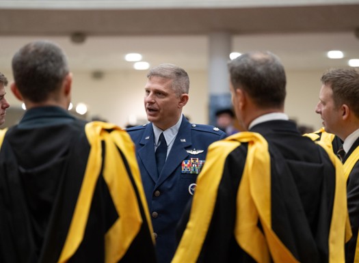 US RAF officer talking to graduates showing the backs of their black and yellow gowns.