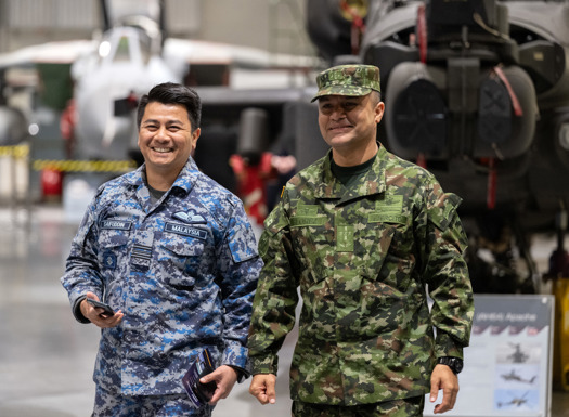 Columbian and Malaysian officers walking through a large hall with a UK military helicopter in the background.