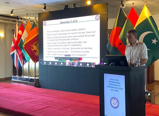 Major General Roe giving a presentation surrounded by international flags.