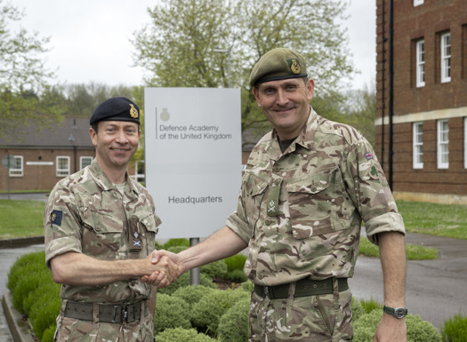Two army officers shaking hands outside a building.