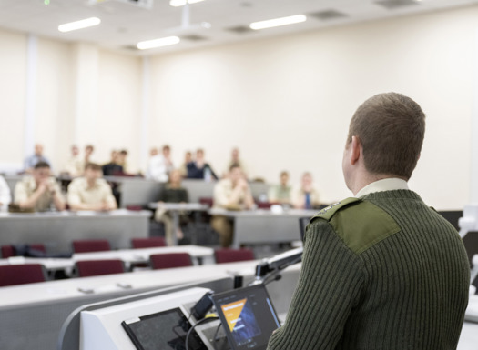 An army officer stood at a lectern presenting to an audience.