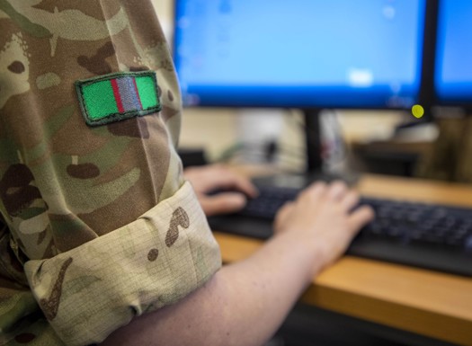 A close-up showing an officer in army combats typing on a computer.