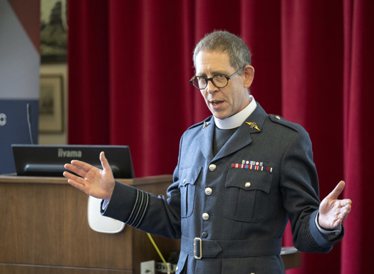 An RAF padre with his arms open addressing an unseen audience.