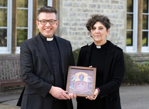 a female and Male Reverand holding a religious artwork.