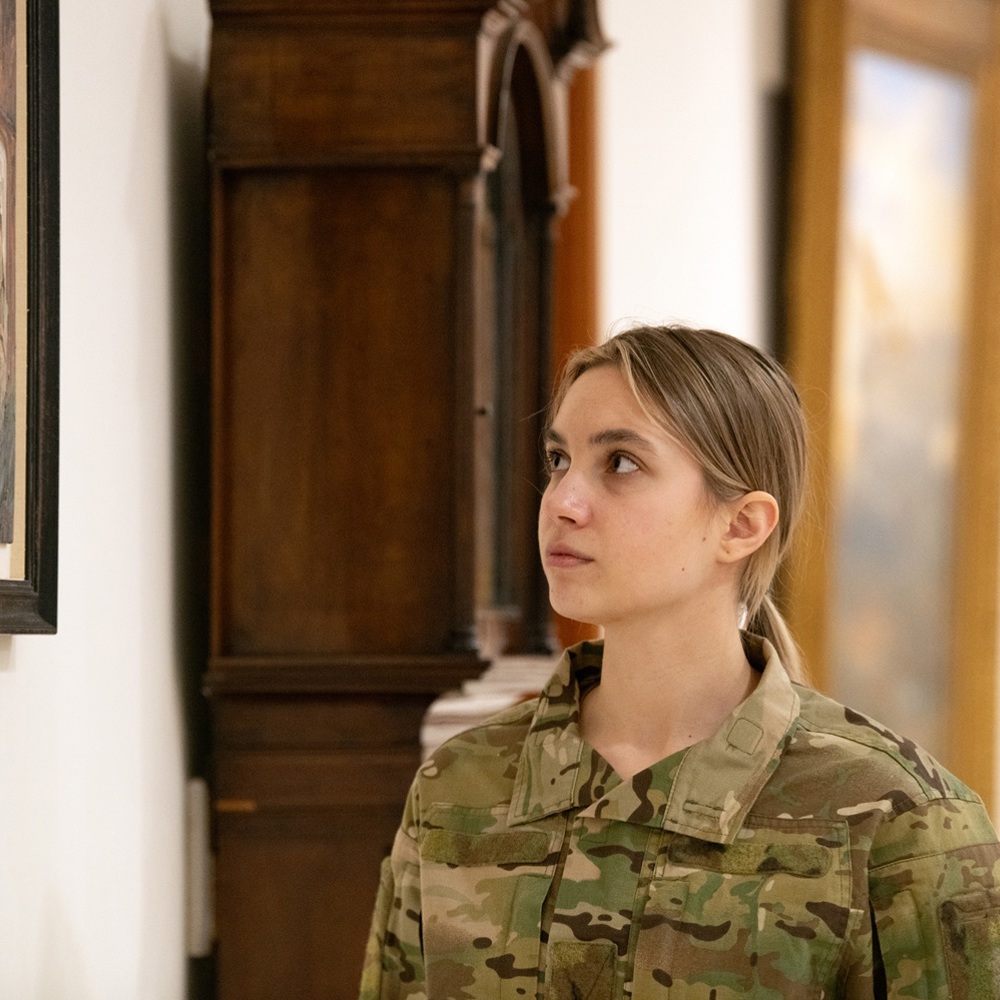 Soldier in camouflage uniform attentively viewing framed artwork in a museum gallery.