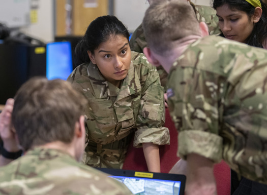Young military student leaning over desk collaborating with peers.