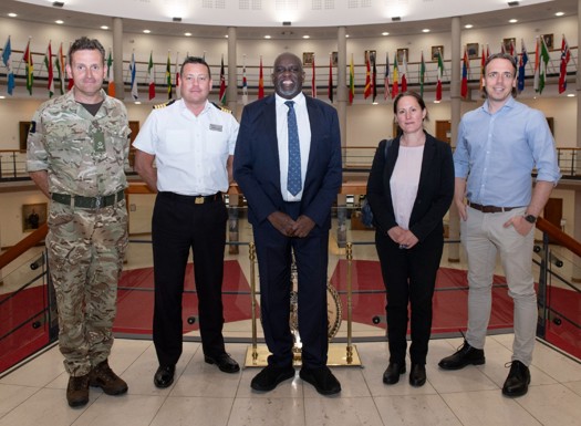 Lord Sewell with military and civilian staff in the Cormorant building forum with international flags in the background.
