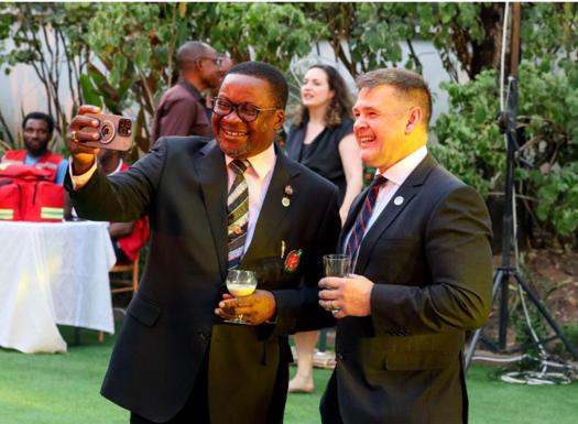 Two men in suits smiling taking a selfie.