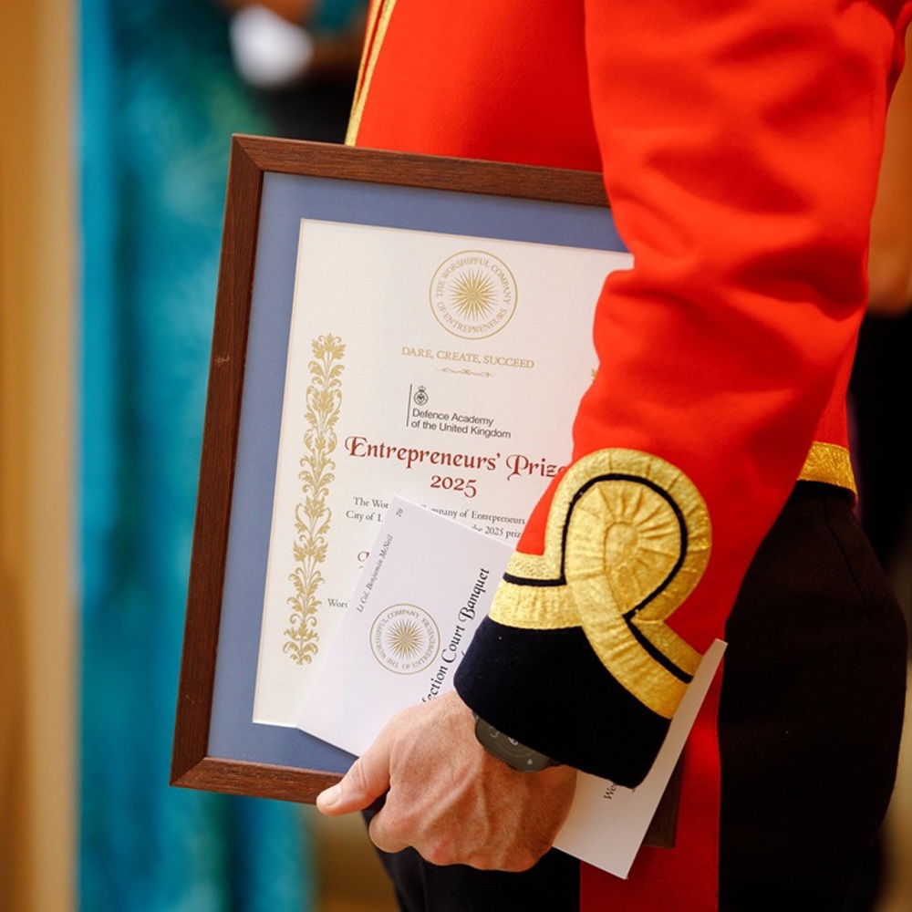 Person in a red ceremonial uniform holding a framed Entrepreneurs Prize 2025 certificate at an award event.