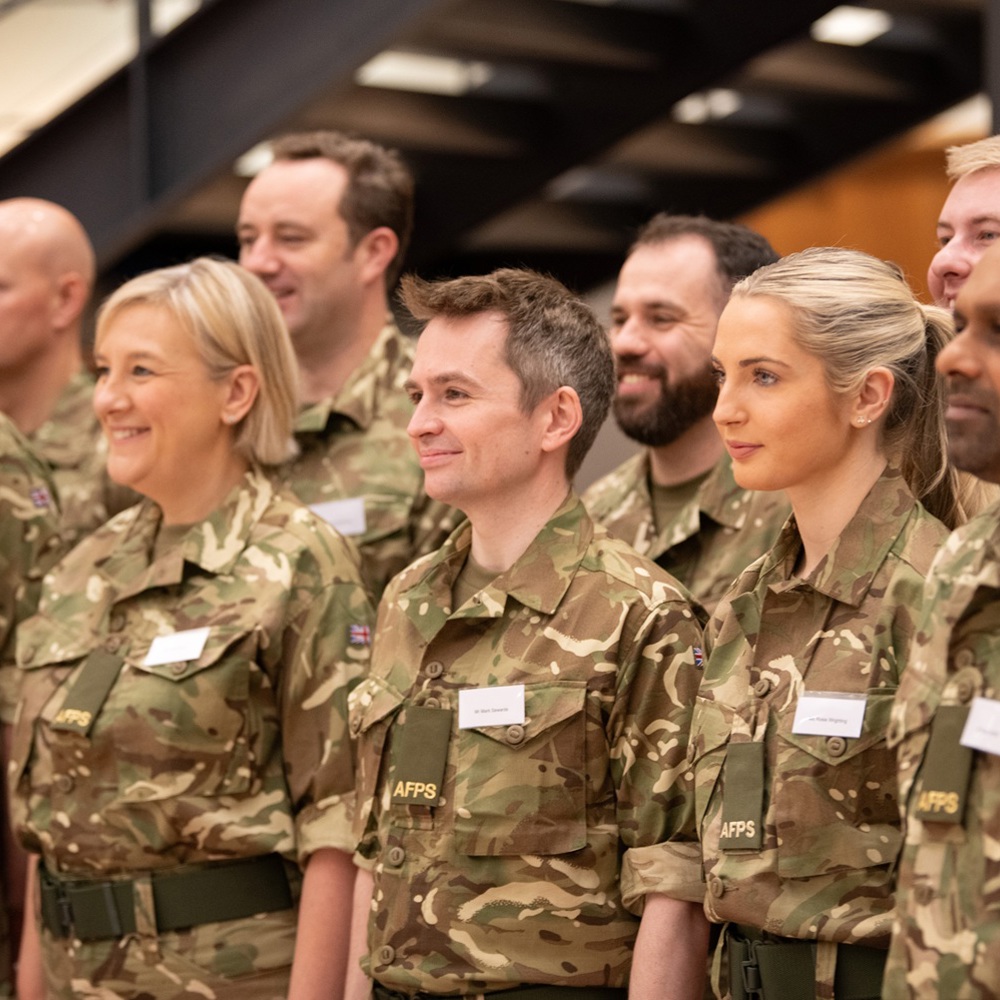A group of smiling individuals in matching camouflage uniforms pose for a photo, all looking side on to the camera.