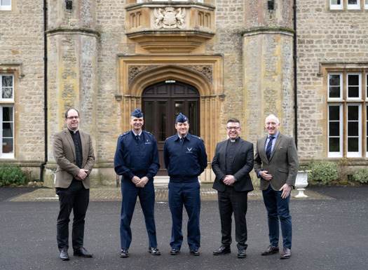 Military Padres and US Air Force officers stood outside an impressive stone grade 2 listed building with a large double wooden door behind them.