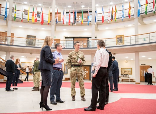 whole force staff gathered in the Forum drinking coffee surrounded by international flags.