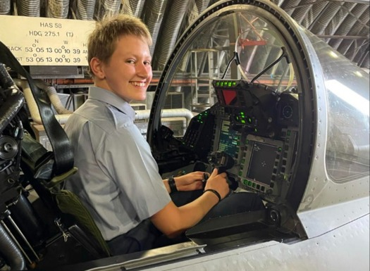 A female officer cadet seated in a cockpit smiling at the camera